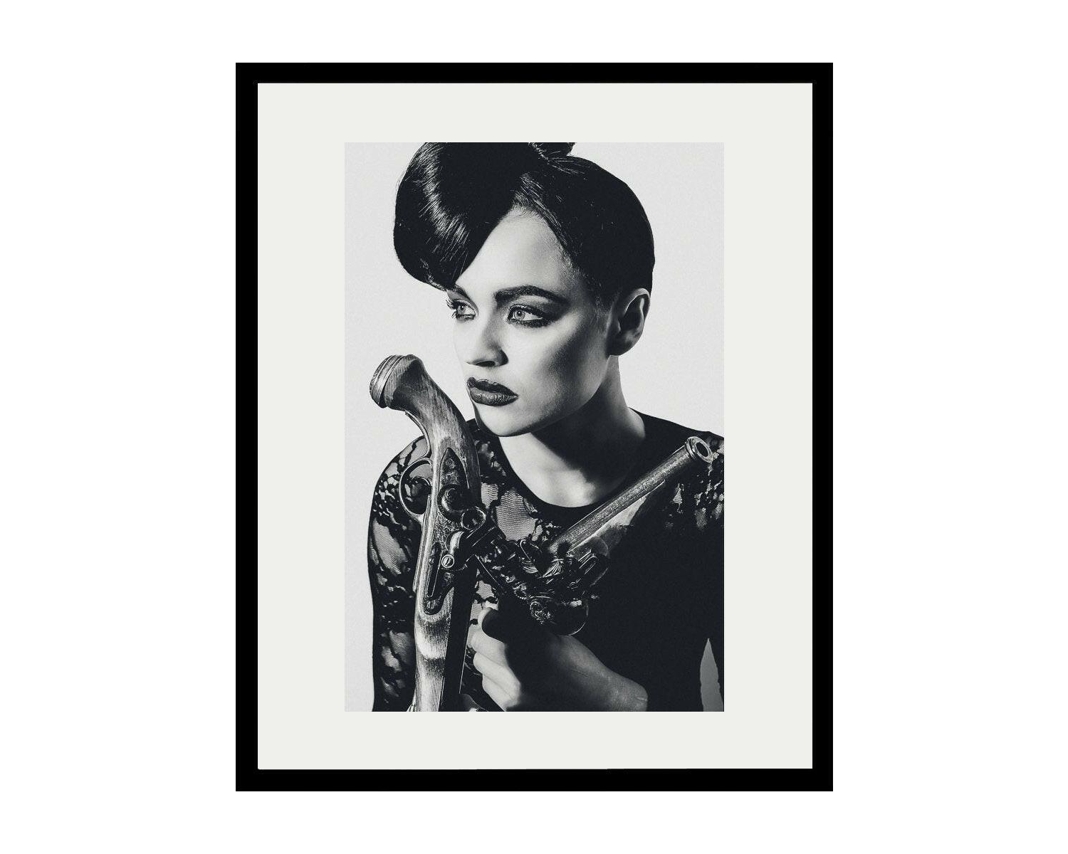 Framed black and white portrait of a woman holding a vintage gun.