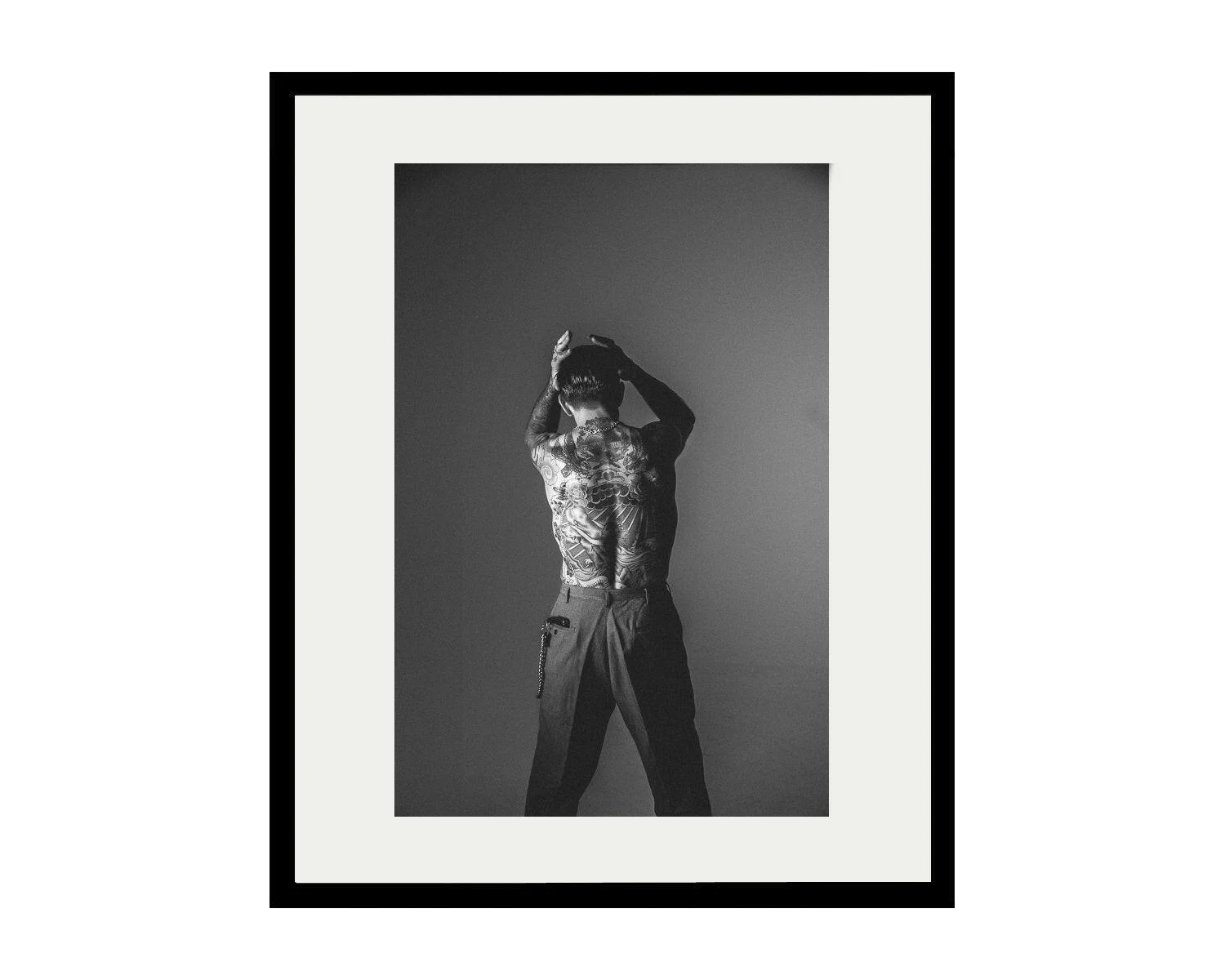 Framed black and white portrait of a person with tattoos on a plain background