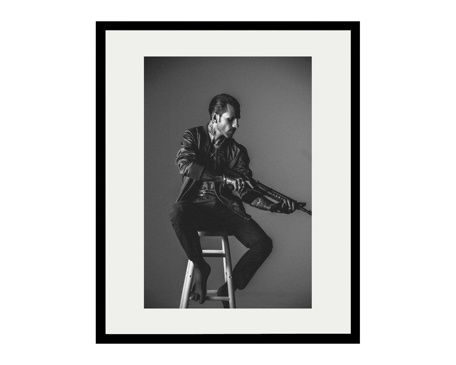 Framed black and white portrait of a man sitting on a stool.