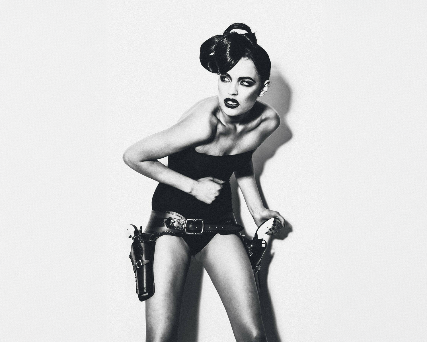 Black and white image of a lady in a stylized outfit with a gun holster on a plain background