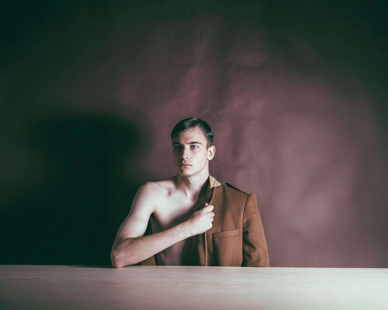 Man in a brown jacket standing against a dark background