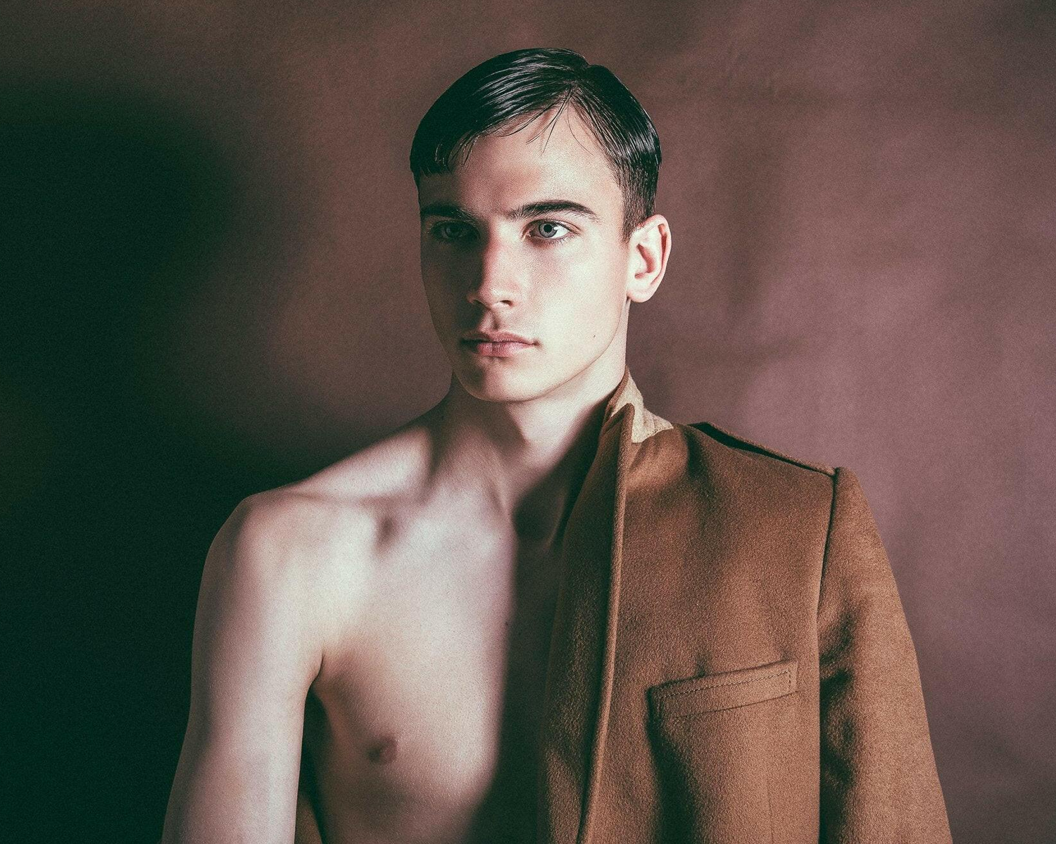 Man wearing a brown jacket against a dark background