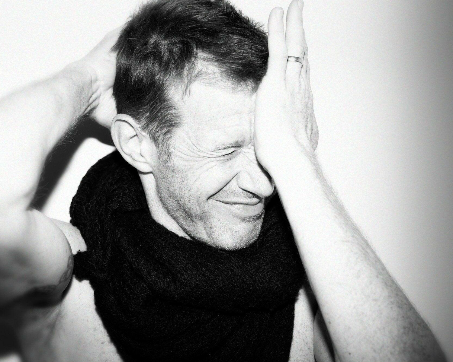 Black and white photo of a man with his arms raised, covering his face.