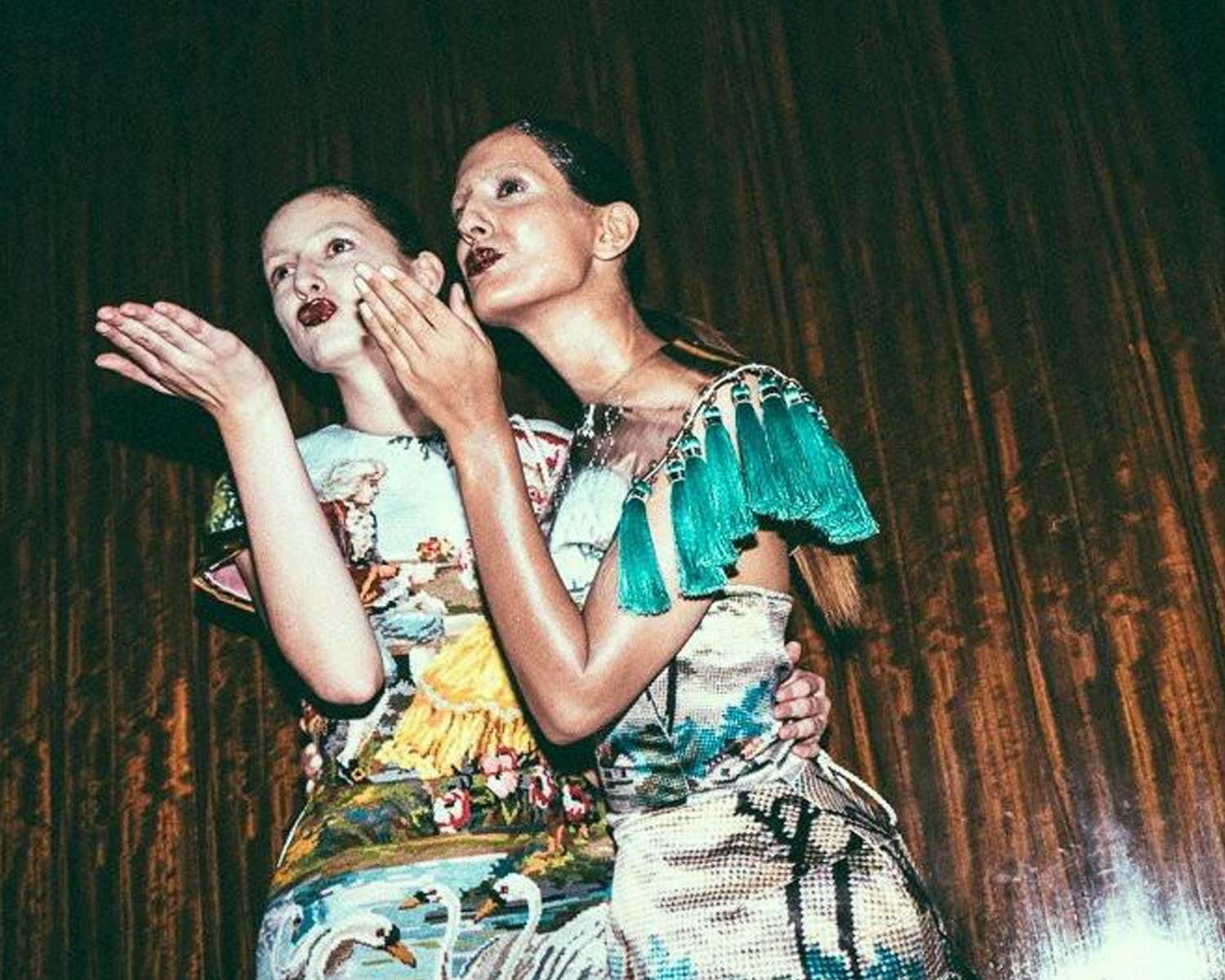 Two women in colorful outfits with a dark background