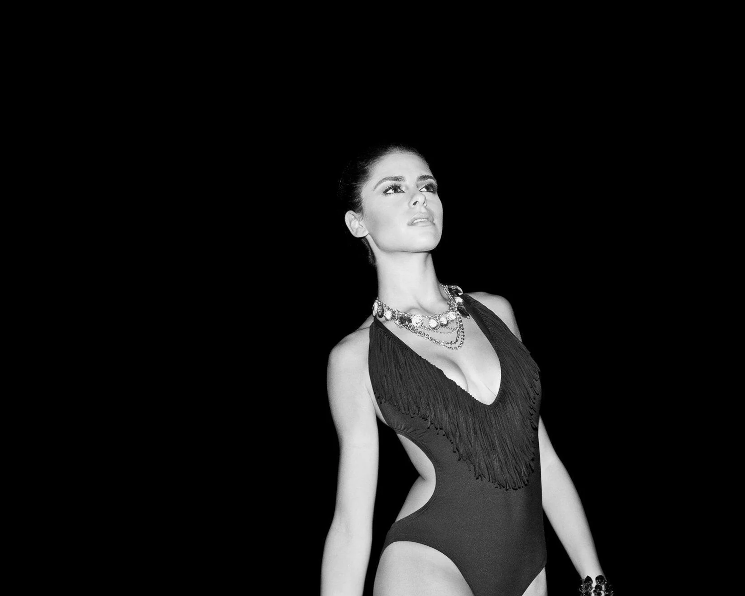 Black and white image of a woman wearing a fringed swimsuit with a necklace.