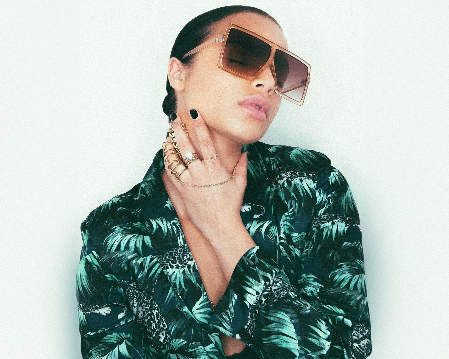Woman wearing sunglasses and a green leaf-patterned shirt against a white background