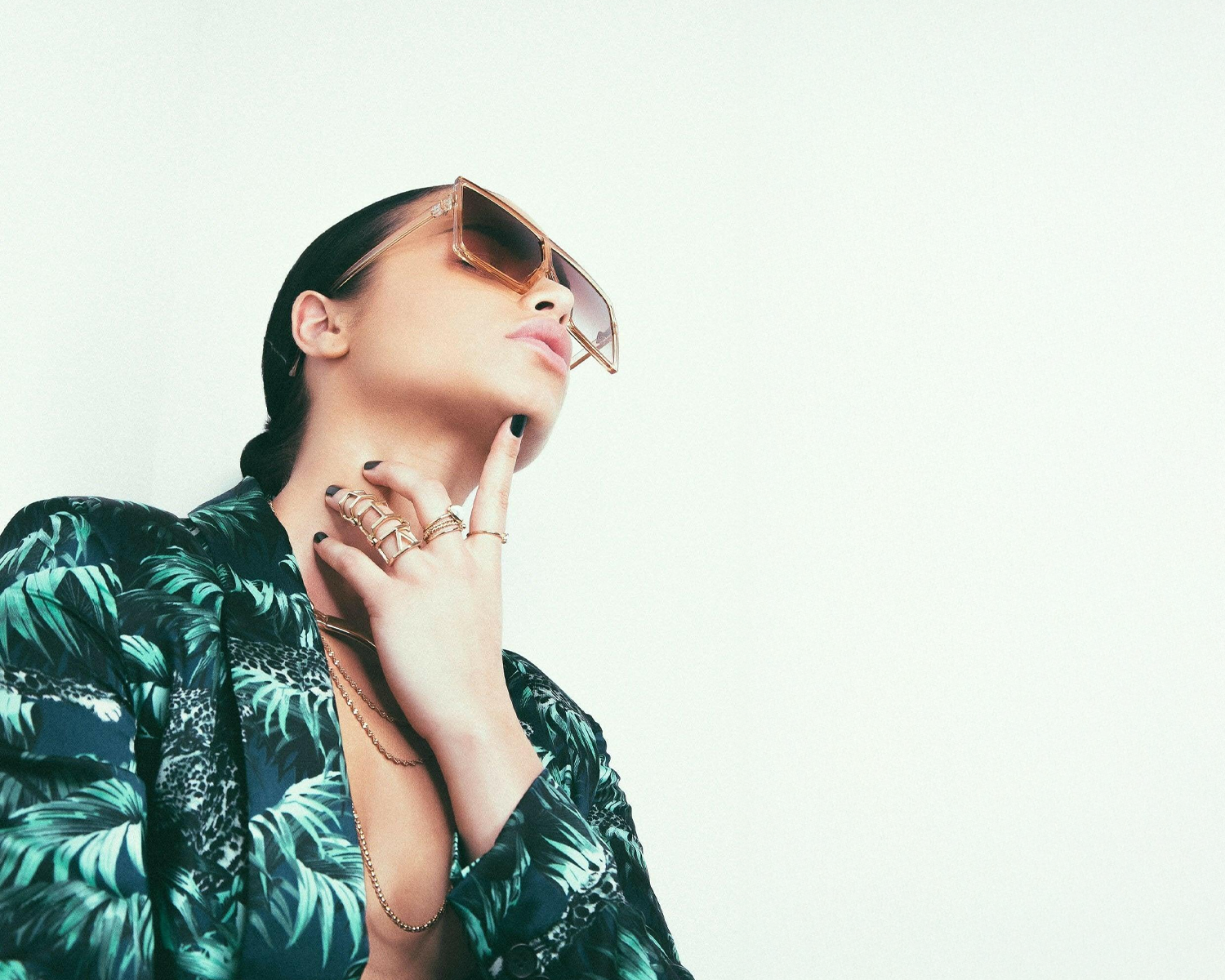 Lady wearing a tropical print shirt and sunglasses with a plain background