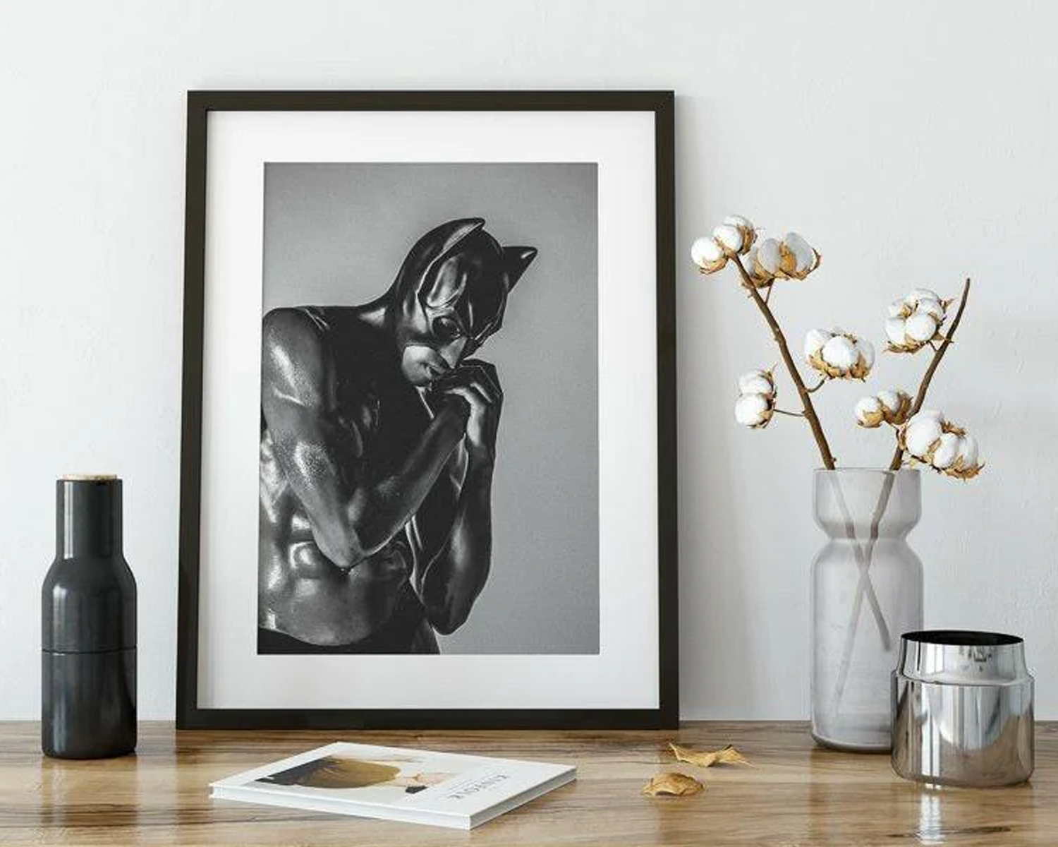 Framed black and white artwork of a nude figure on a wooden table with decorative items.