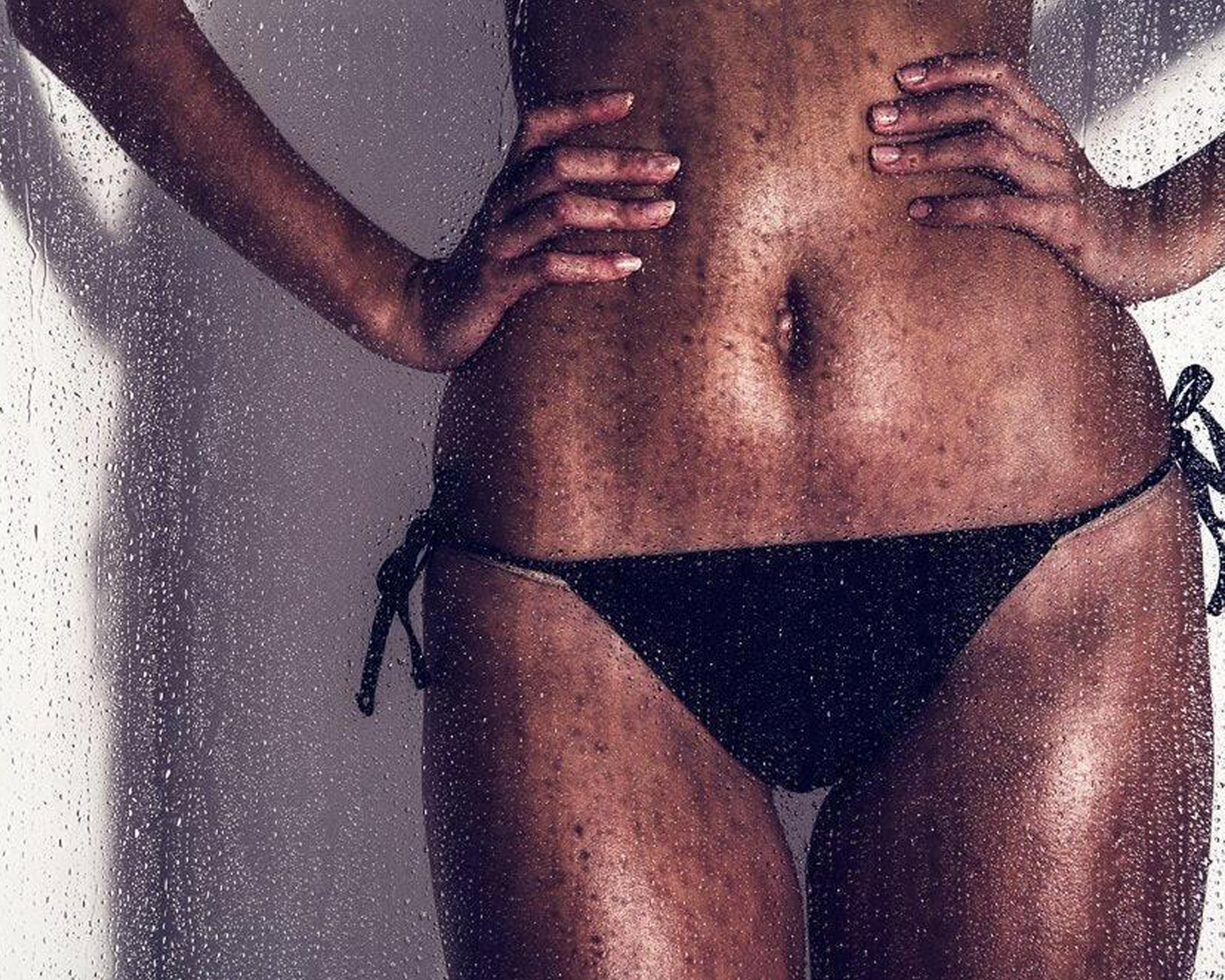 Girl wearing a black bikini with hands on hips against a gray background