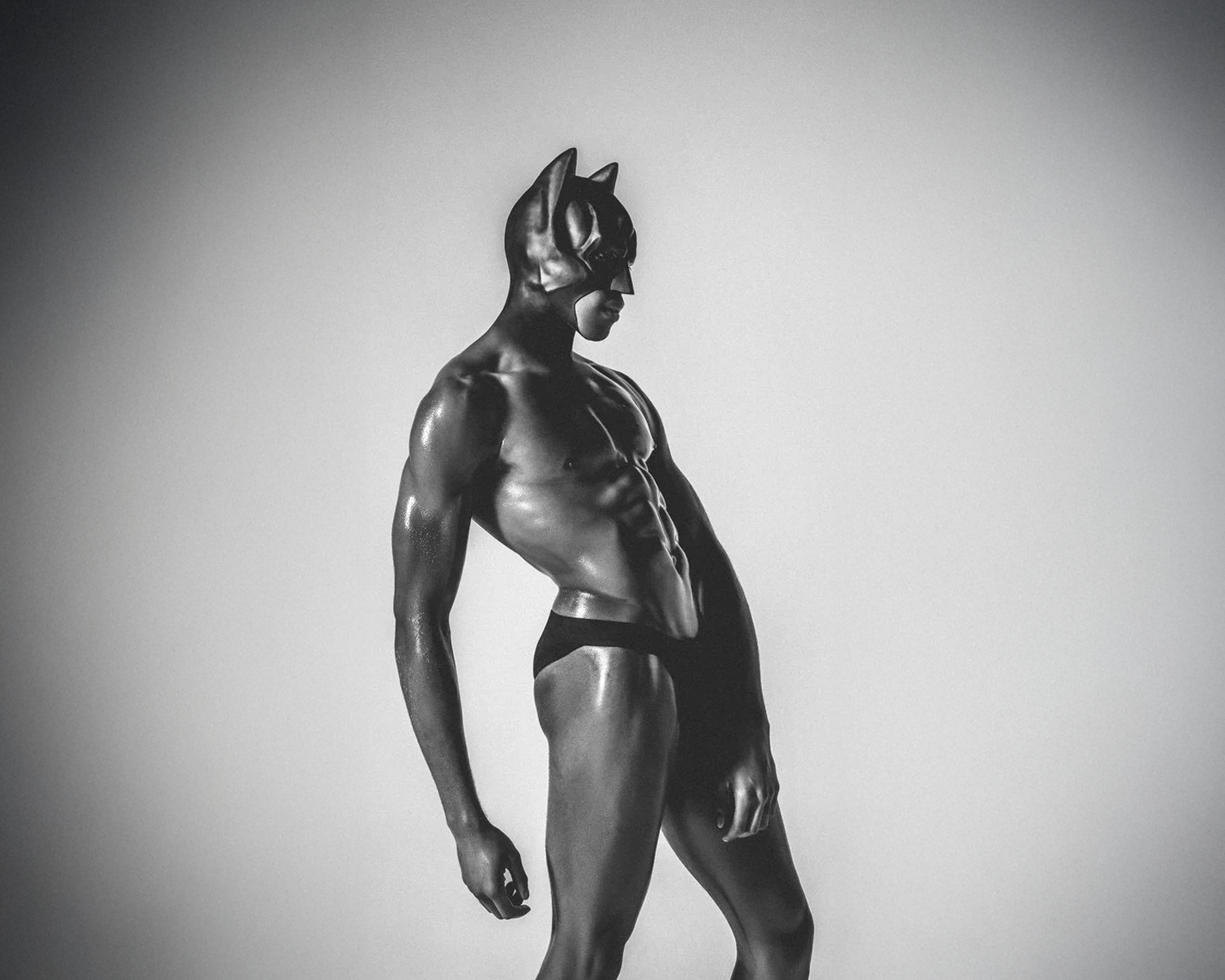 A muscular figure in a black mask and minimal attire poses dramatically against a neutral background, conveying strength and intensity.