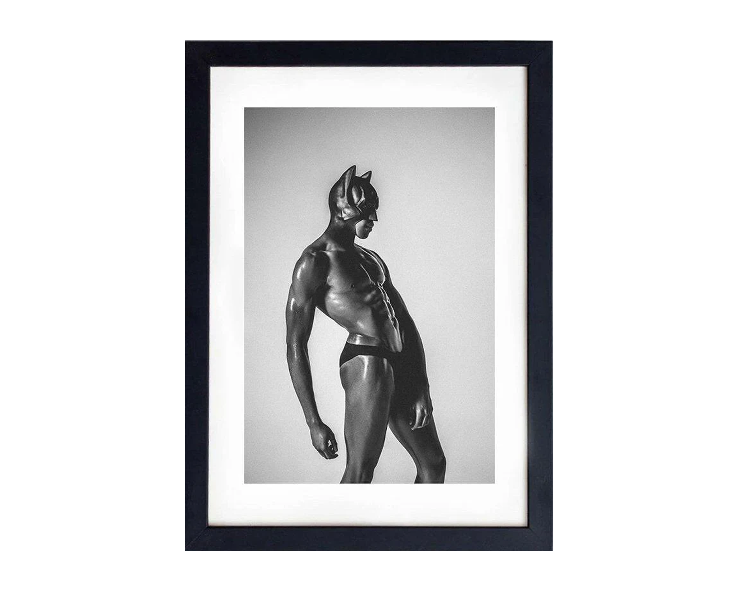 Framed black and white photograph of a muscular figure in a black mask and minimal attire poses dramatically against a neutral background, conveying strength and intensity.