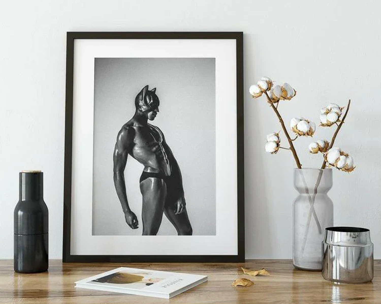 Framed black and white art print of a muscular figure on a wooden surface with decorative items.