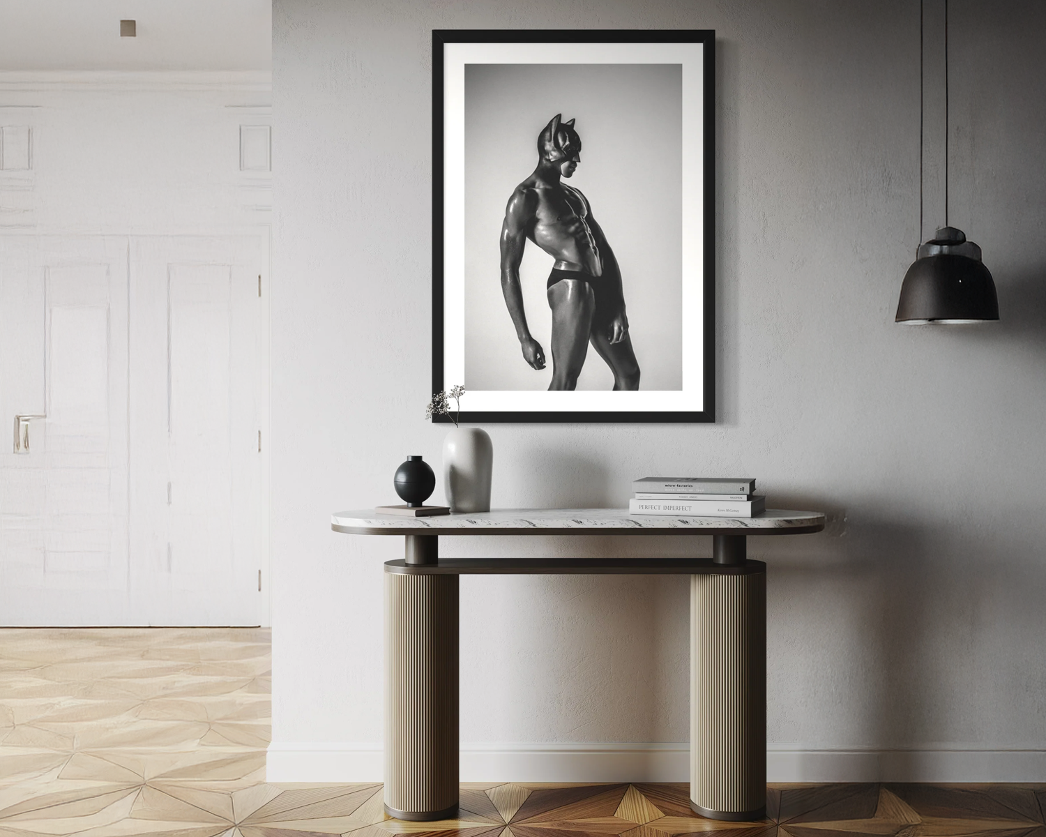 Framed black and white artwork of a muscular figure on a wall above a console table.