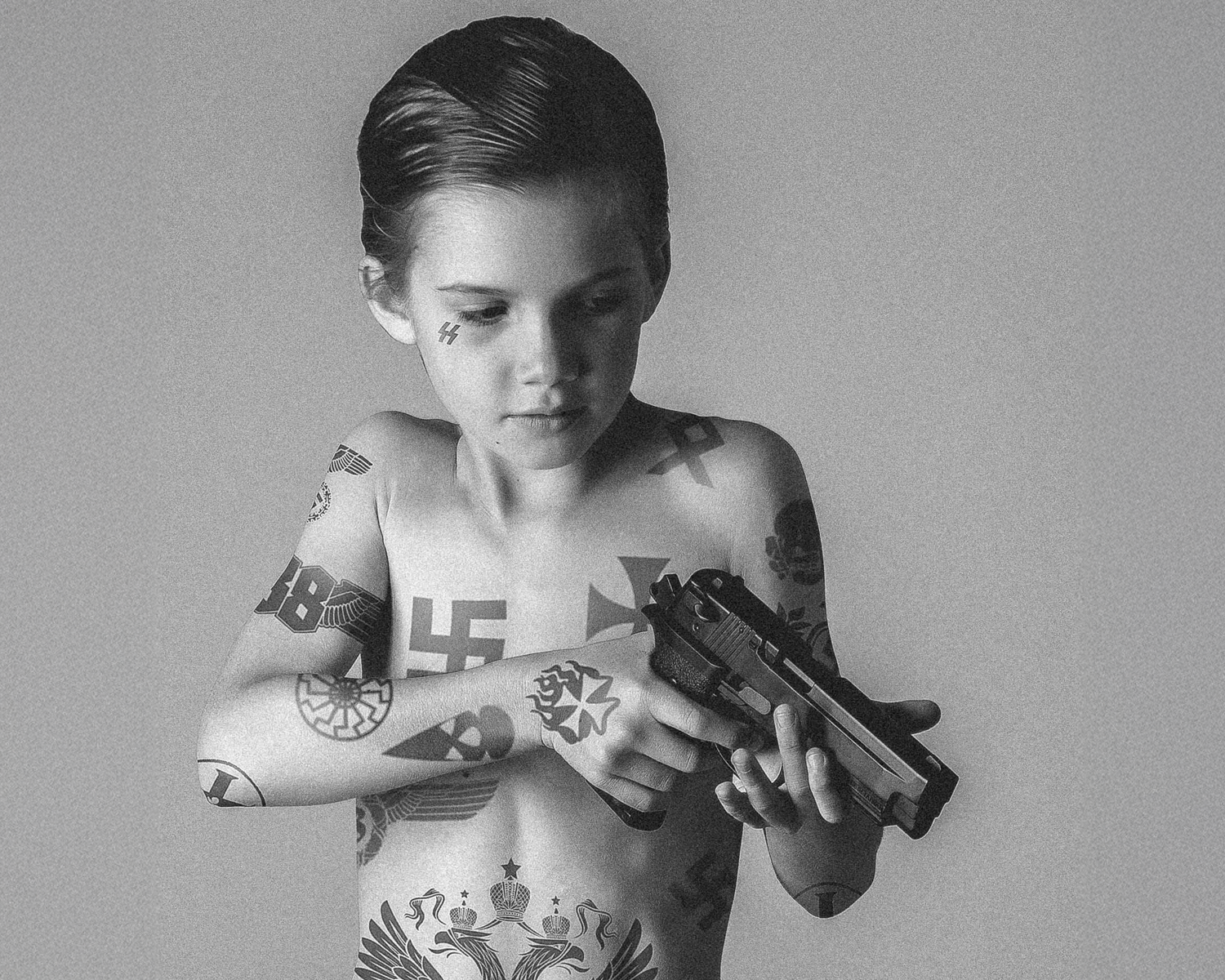 Black and white photo of a child with tattoos holding a gun.