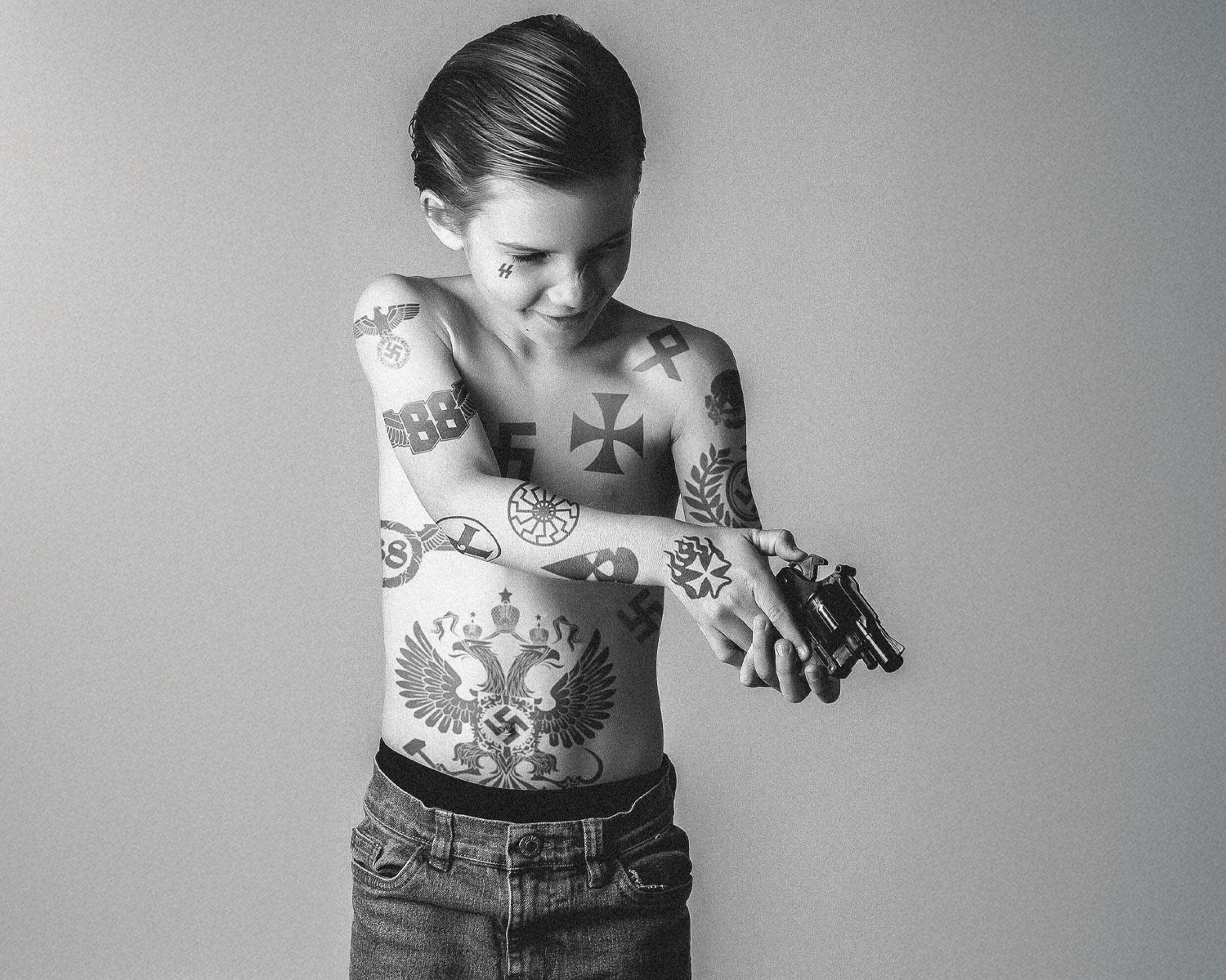 Black and white photo of a child with tattoos holding a toy gun.