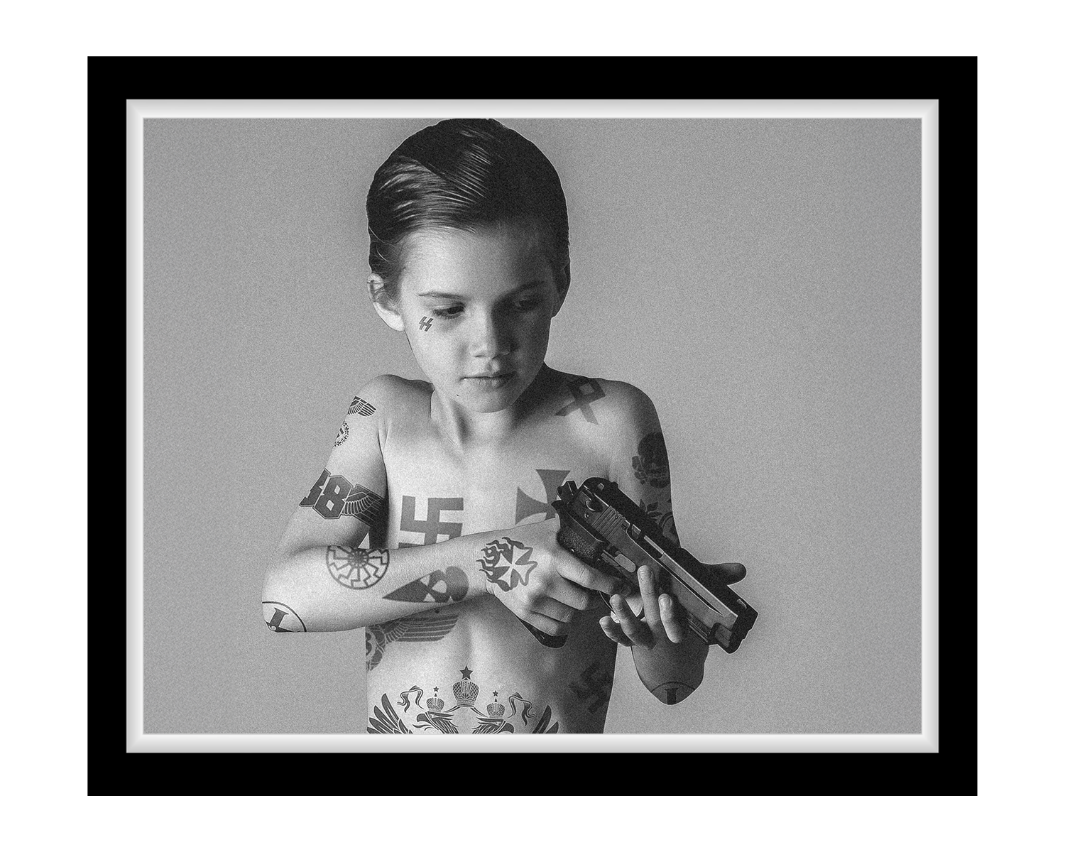 Black and white photo of a child with tattoos holding a gun against a plain background