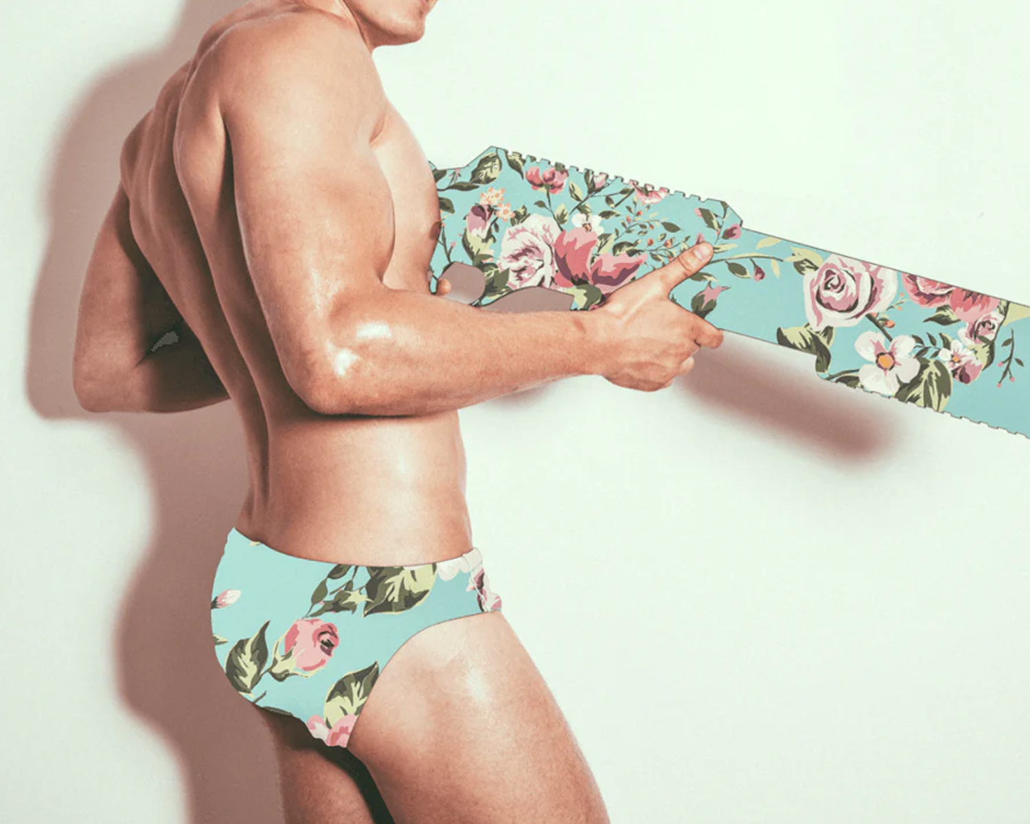 Man wearing floral underwear holding a floral-patterned gun against a light background