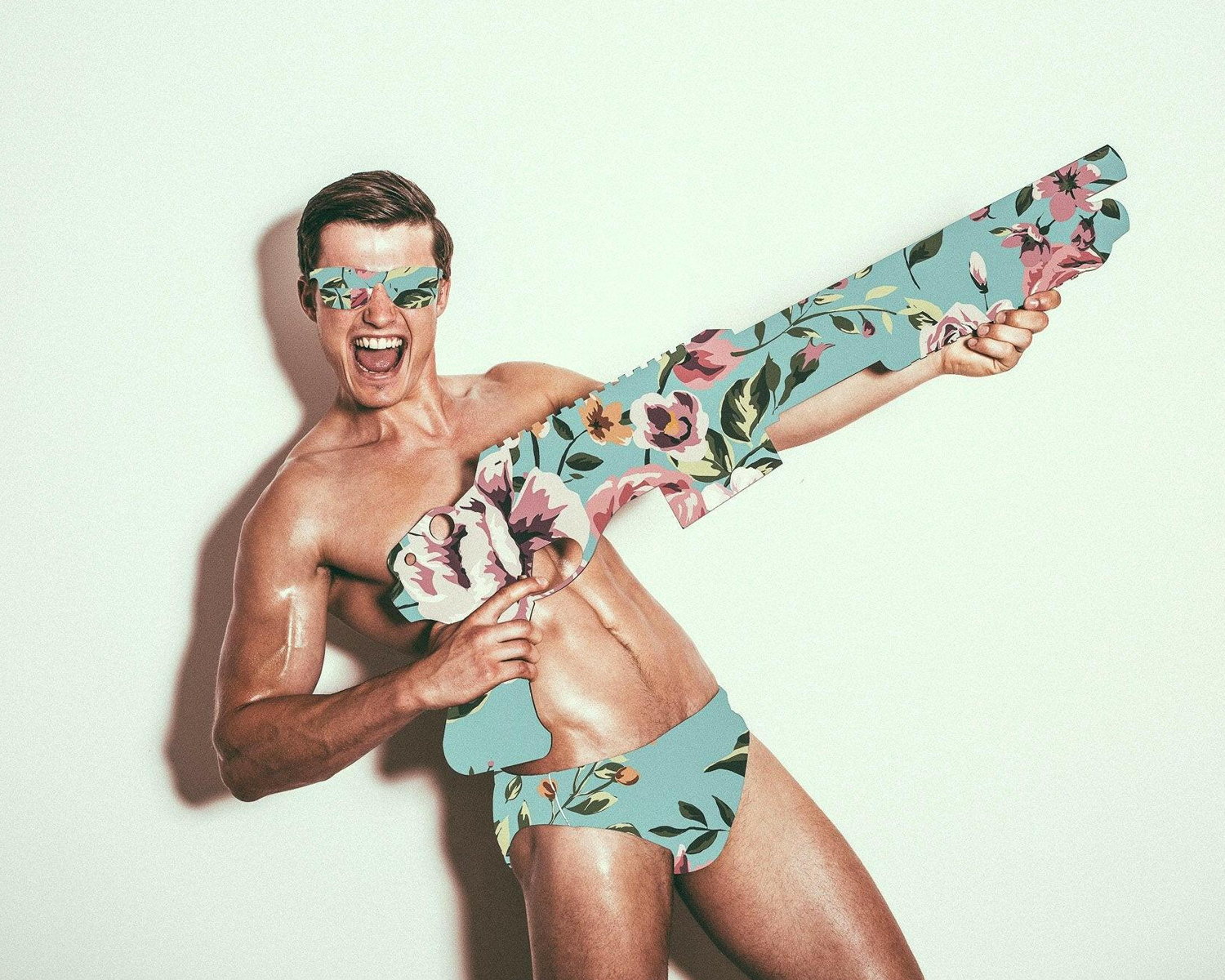 Man wearing a floral swimsuit and holding a floral-patterned gun against a white background