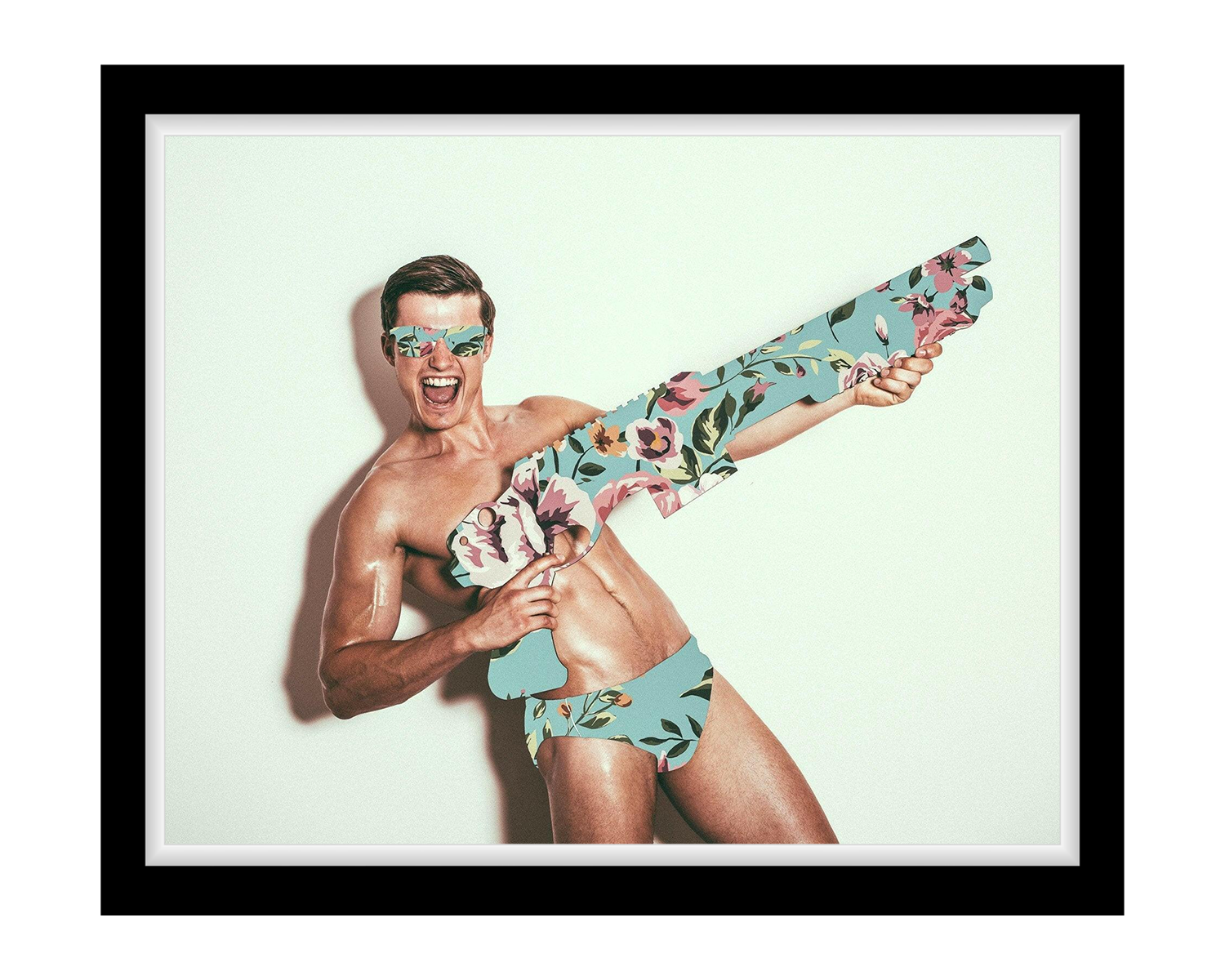 Man wearing a floral swimsuit and sunglasses holding a floral-patterned gun against a light green background.
