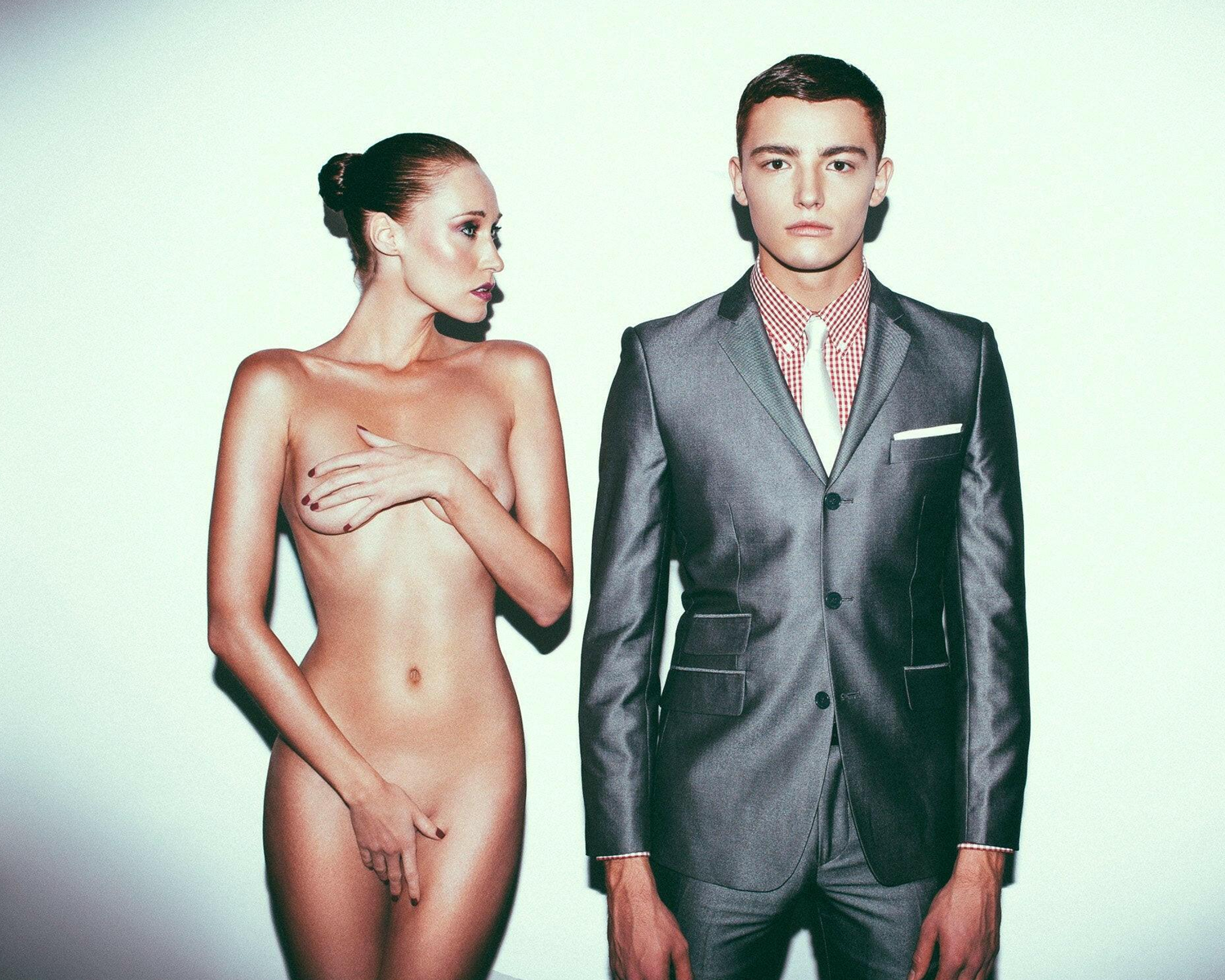 Man in a suit standing next to a nude woman on a white background
