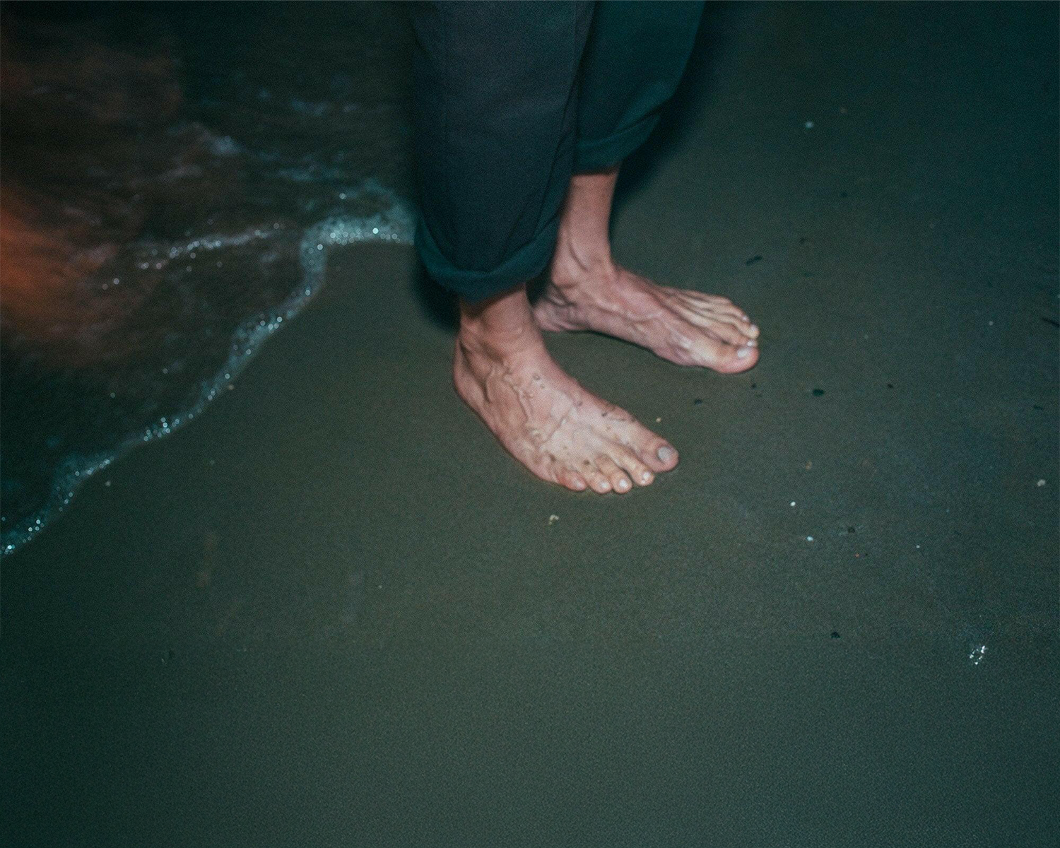 Feet standing on a beach with water at the base of the feet.