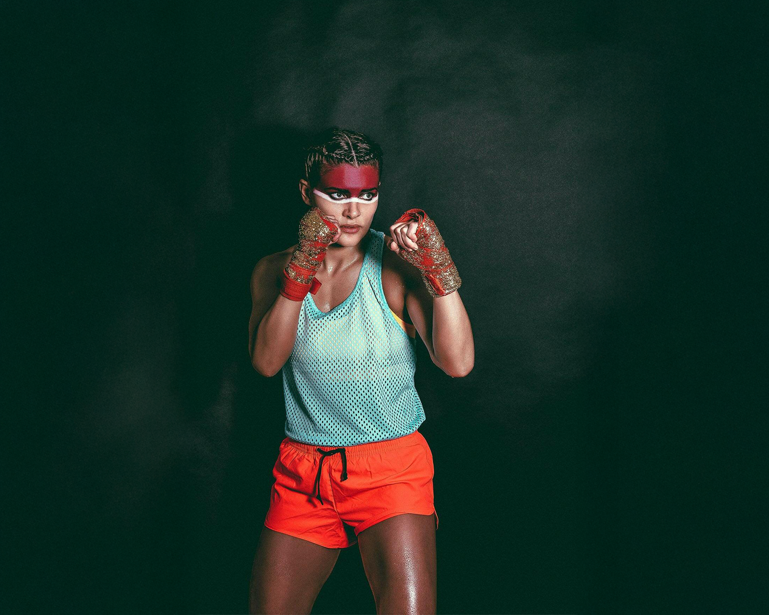 A woman wearing orange shorts and a blue tank top stands confidently, showcasing a vibrant summer outfit.