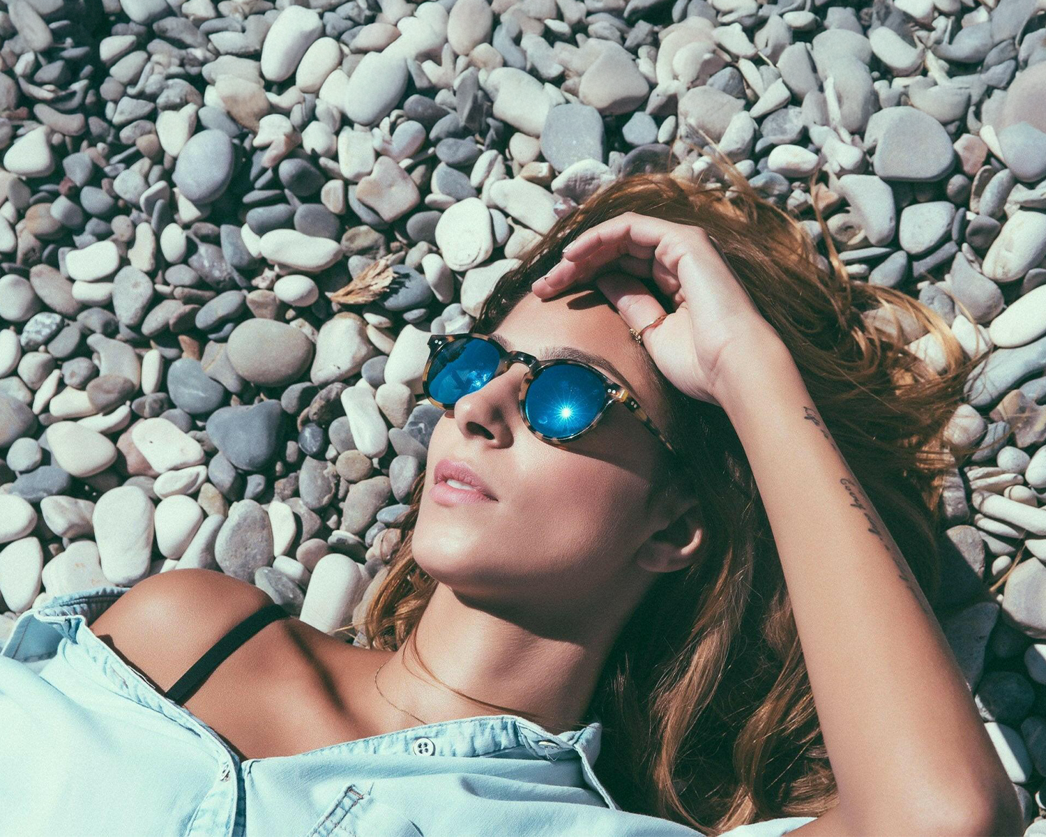 Woman wearing sunglasses lying on pebbles by the sea