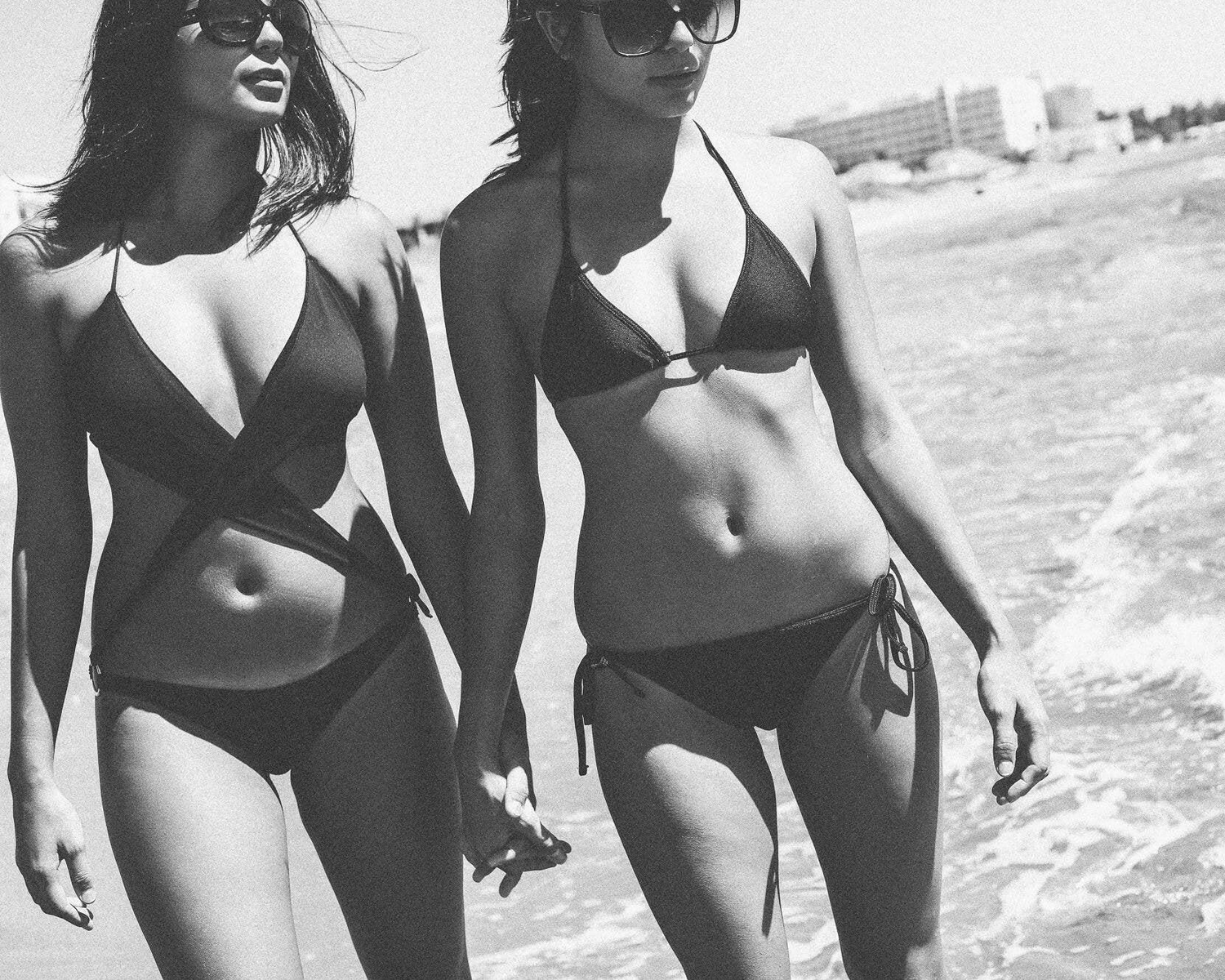 Two women in black swimsuits walking on a beach.