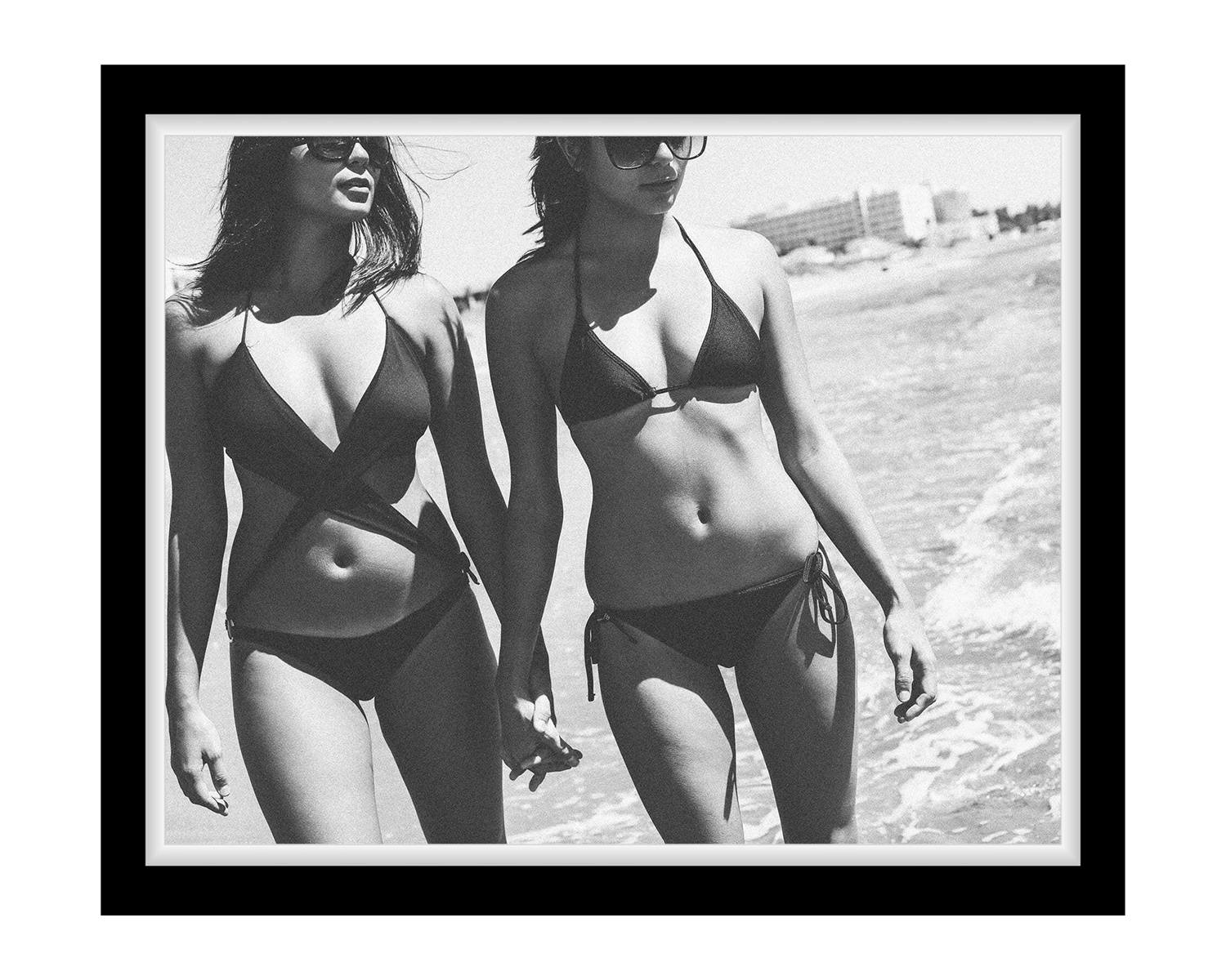 Two women in black bikinis walking on a beach.