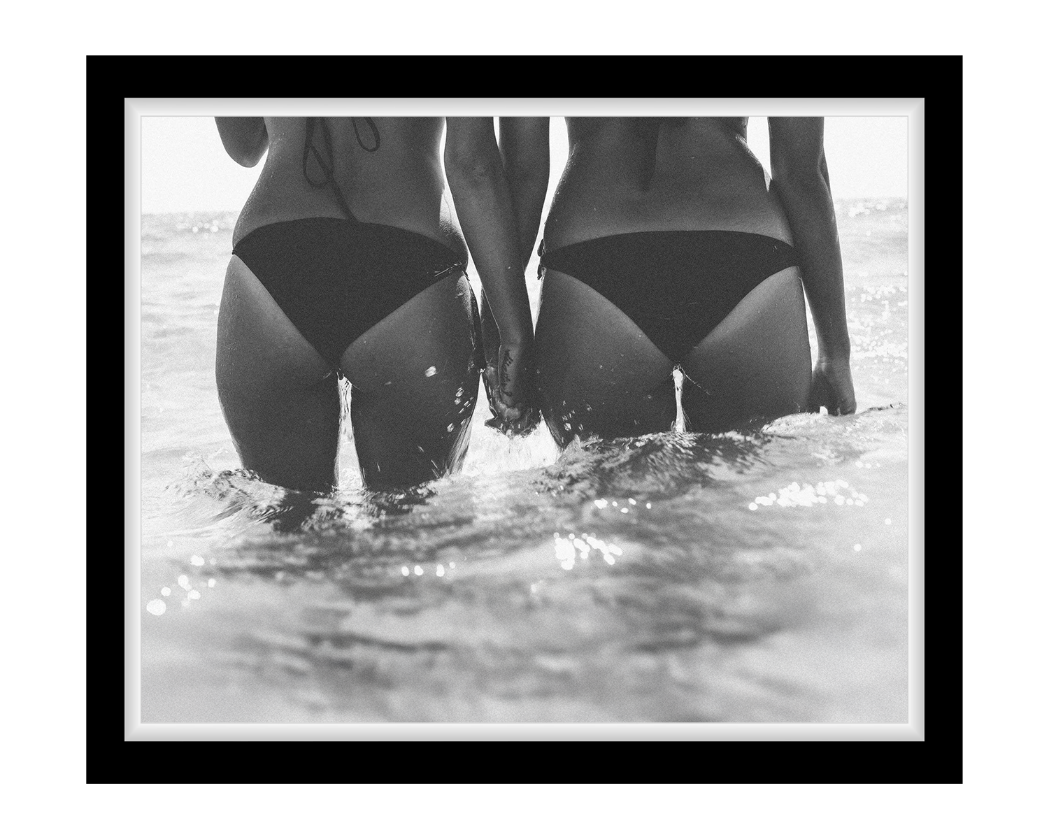 Two women in black swimsuits standing in water, framed with a black border.