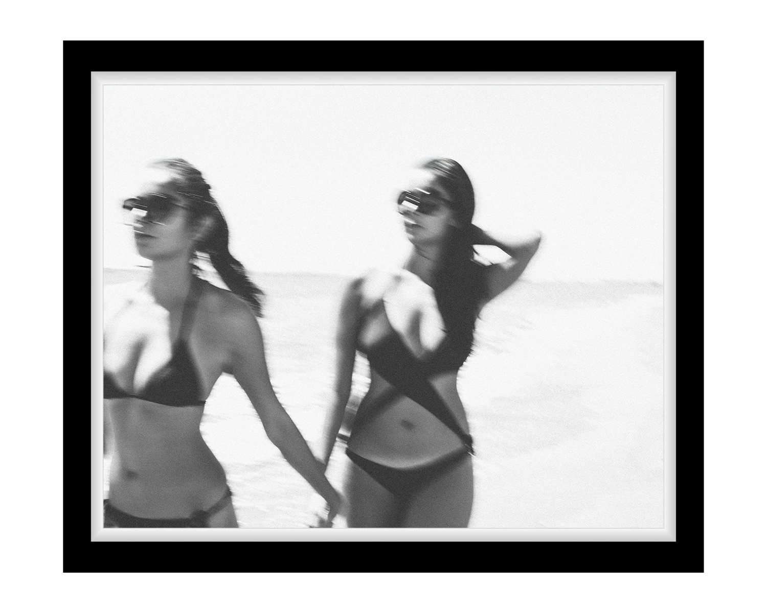 Two women in swimsuits walking on a beach with a black frame.