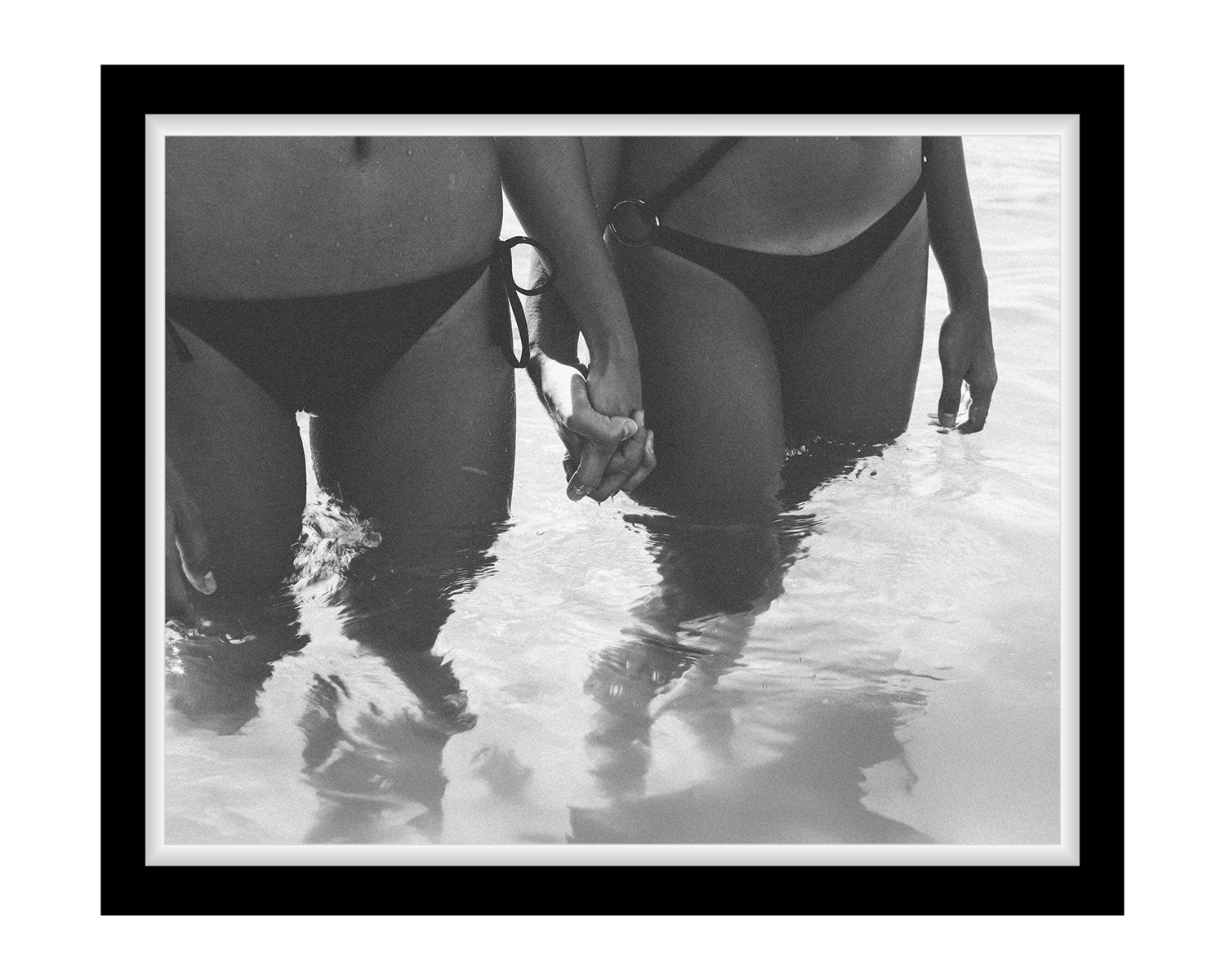 Two people in swimsuits walking through shallow water on a beach.