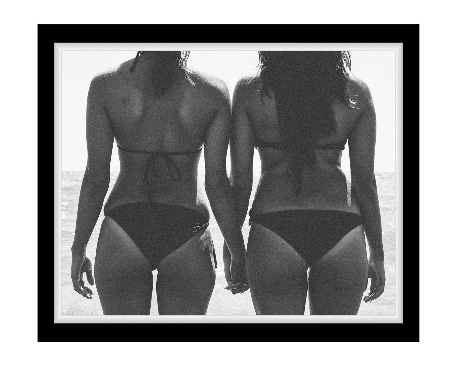 Two women wearing black swimsuits standing back-to-back with a blurred background