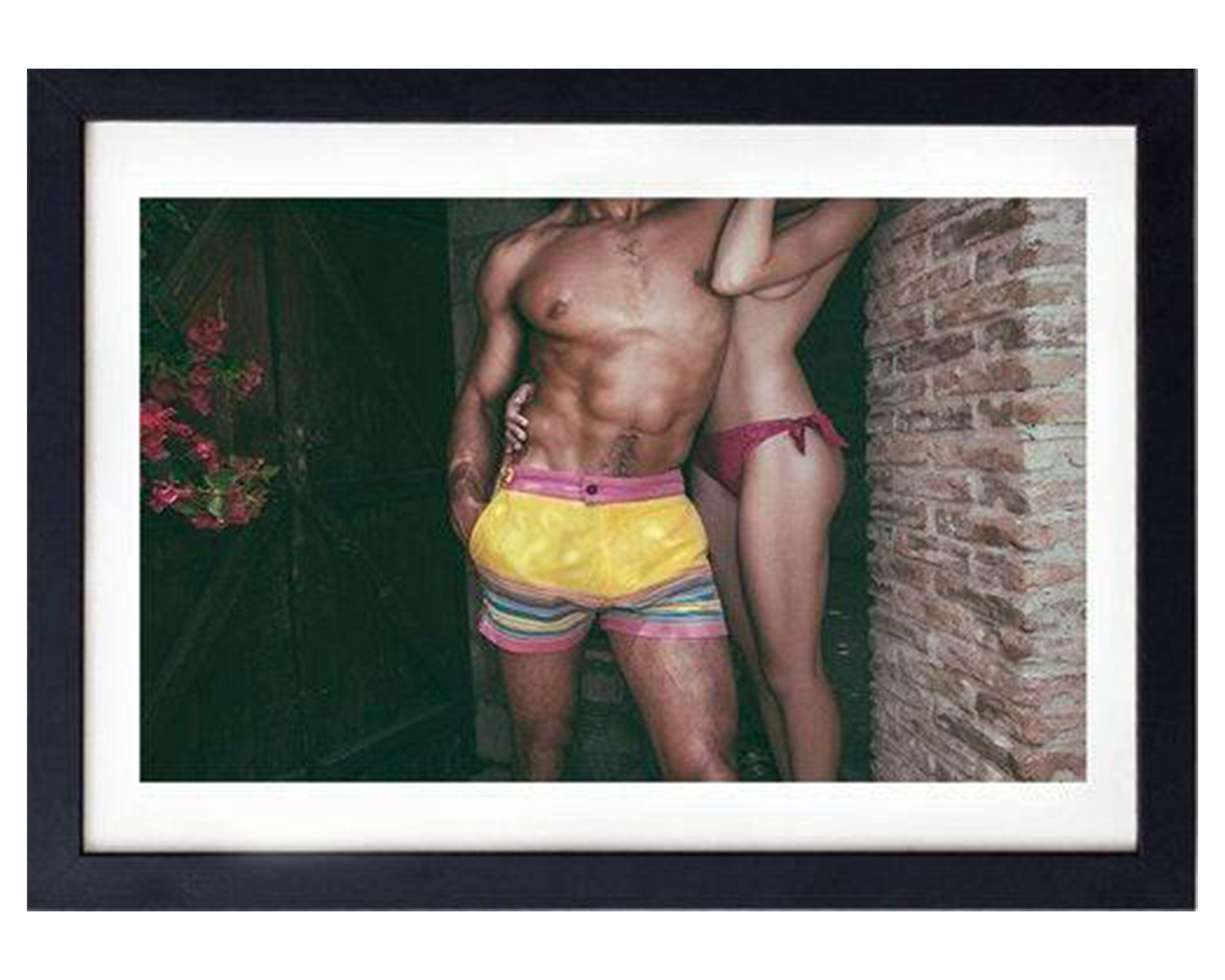 Framed photograph of a man and woman in colorful swim trunks, standing side by side and posing for a cheerful photo outdoors.