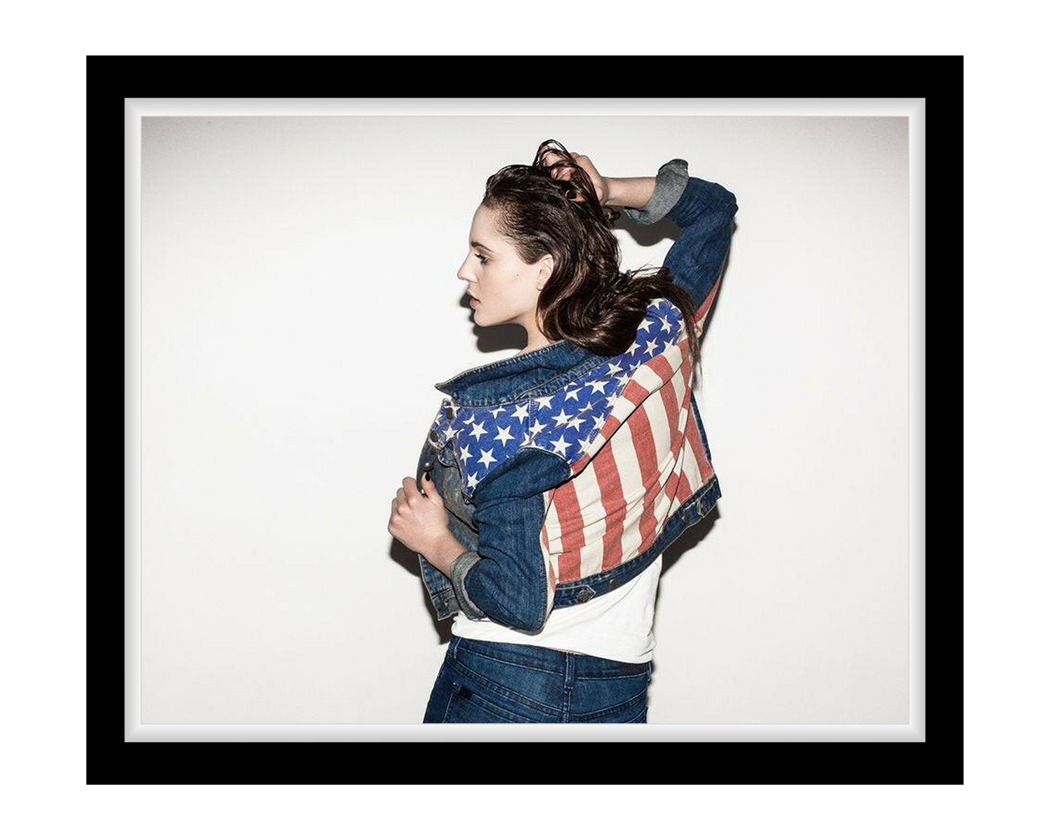 Person wearing a denim jacket with an American flag design on a plain background
