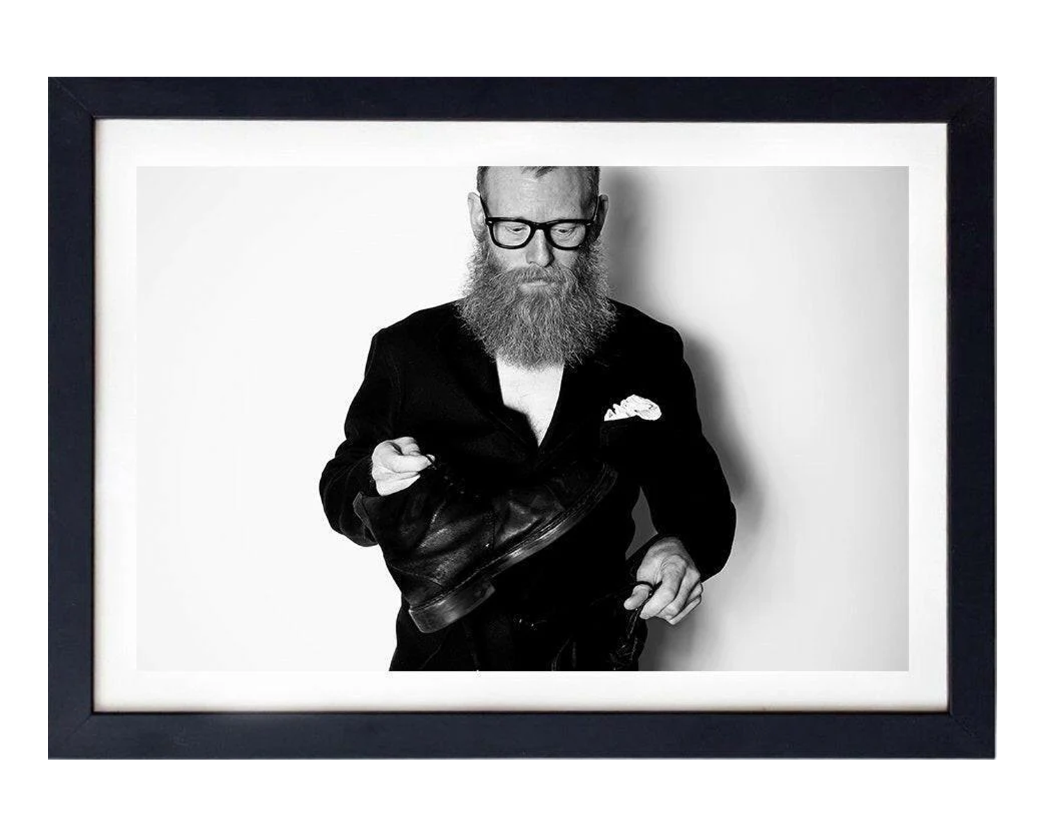 Man in a suit with a beard and glasses holding a leather jacket, framed in black, framed in black.