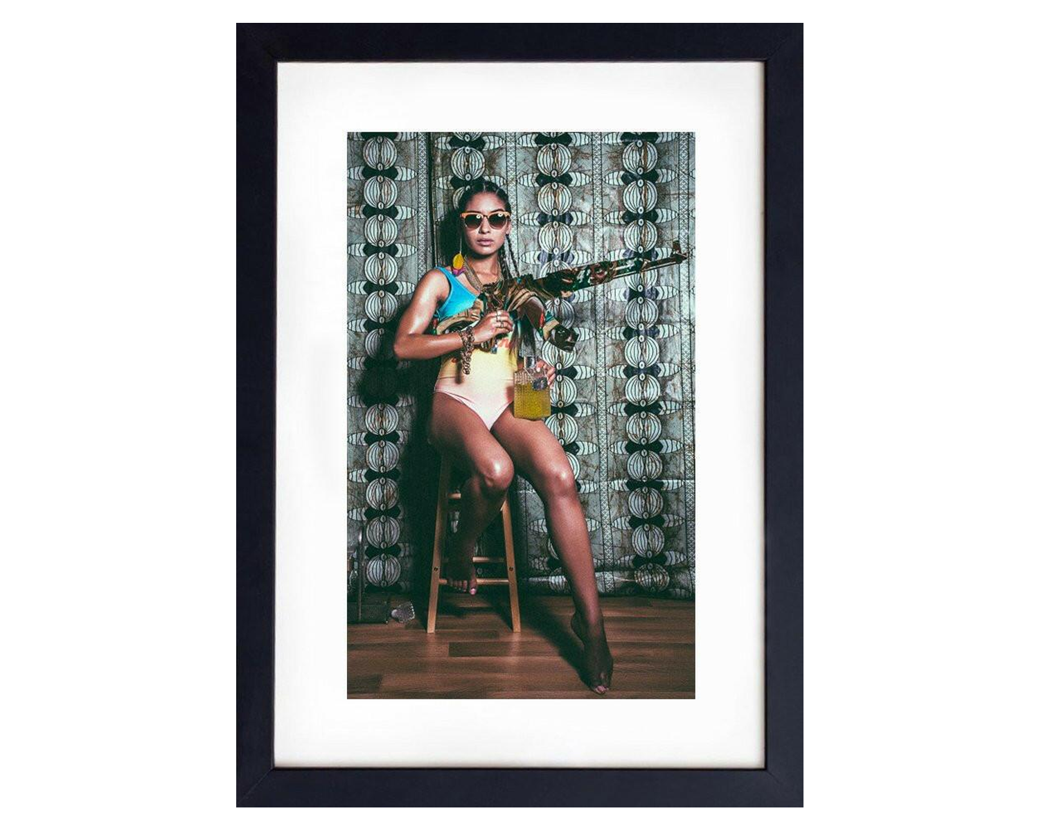 A woman in a swimsuit poses with a gun, showcasing a striking contrast against a sunny beach setting, framed in black.