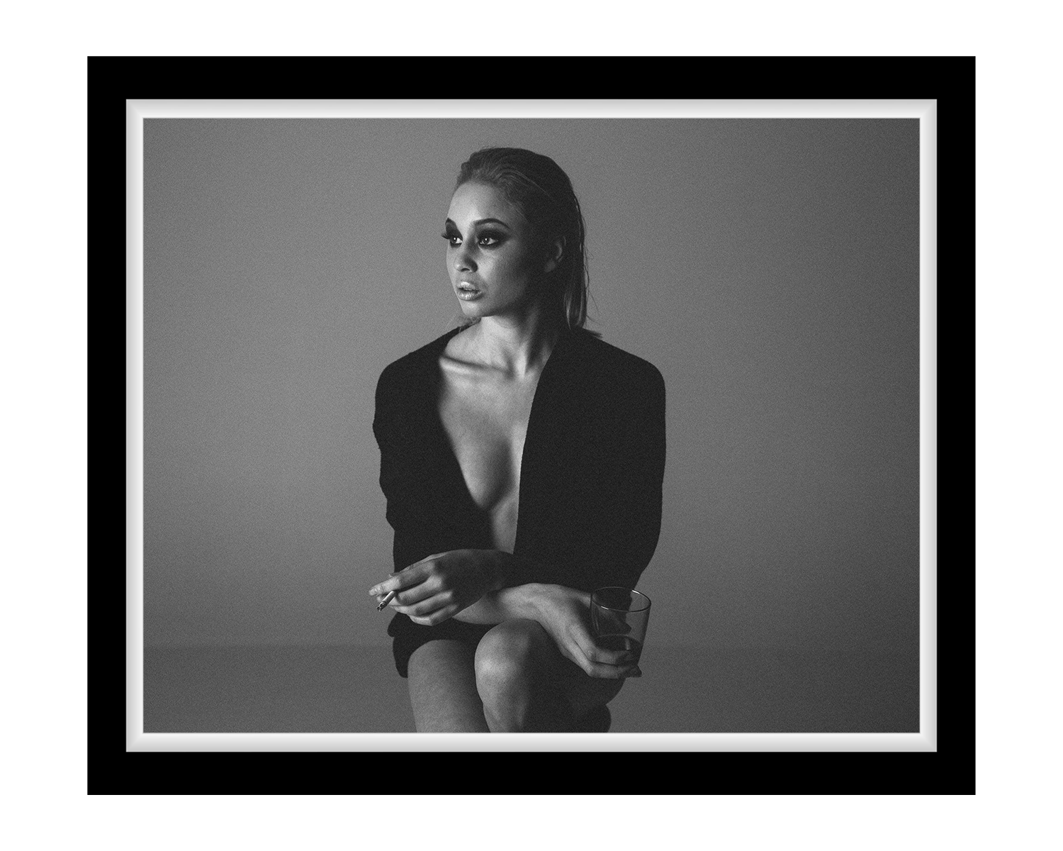 A woman seated on a chair, casually holding a cigarette, with a thoughtful expression, framed in black.